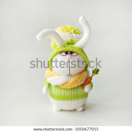 Handmade knitted toy.  Easter Bunny in a green sweater and hat with pompom with carrots in his paw