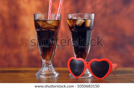 Pouring cola soft drink on ice in tall cafe glasses against a rustic wood background.