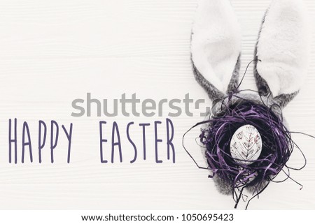 Happy Easter text. season's greetings card. bunny ears and stylish egg in nest on white wooden background flat lay. happy easter concept