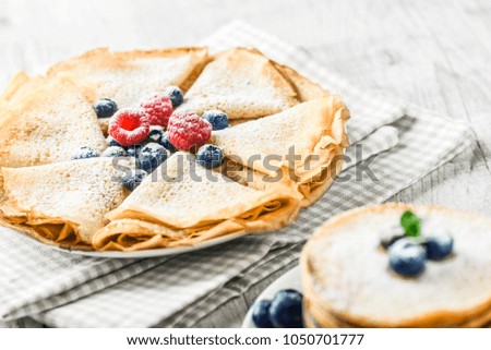 Fried pancakes with forest fruits and mint leaf. Thin flat cakes and blueberries, raspberries. Sweet cake on white plate. 