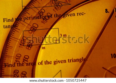 Math still life with protractor and math problems. Clear protractor laying on an open math book. Half moon ruler used in algebra question. Studying math in school.