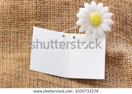 White empty card on brown sackcloth with white flower background to replace your design.