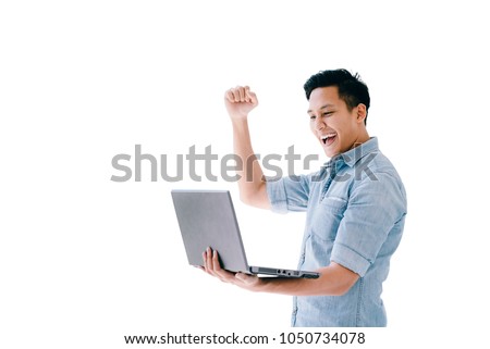 Happy excited Asian man holding laptop and raising his arm up to celebrate success or achievement isolated on white. image with clipping path. Royalty-Free Stock Photo #1050734078