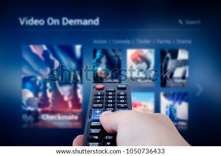 VOD service screen with remote control in hand. Video On Demand television internet stream multimedia concept Royalty-Free Stock Photo #1050736433