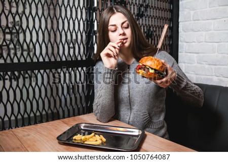 Young girl holding in female hands fast food burger, american unhealthy calories meal on background, hungry person smiling with grilled hamburger