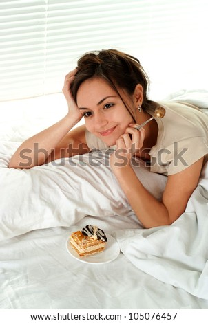Beautiful happy female lying on a bed with a cake on a light background