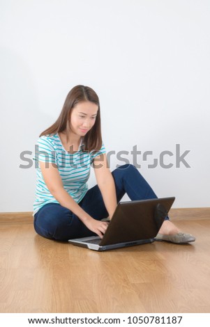Smiling young woman using a laptop on wooden floor and white wall