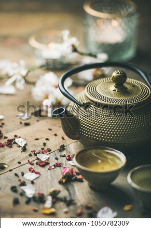Traditional Asian tea ceremony arrangement. Iron teapot, cups, blooming almond flowers, dried rose buds and candles over wooden table background, selective focus