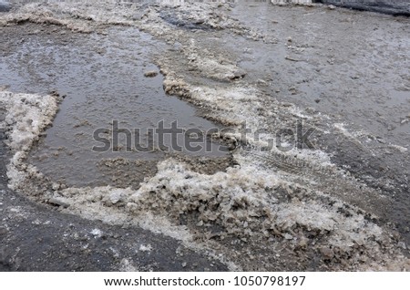 Damaged asphalt road with potholes caused by freezing and thawing cycles during the winter. Poor road