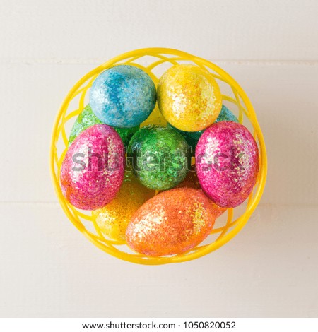 Basket with colorful eggs on a white wooden table. The view from the top.