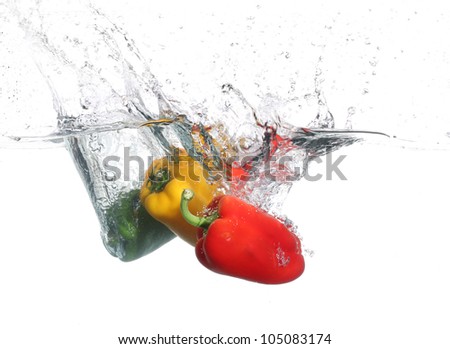 Three peppers falling into water, over white background