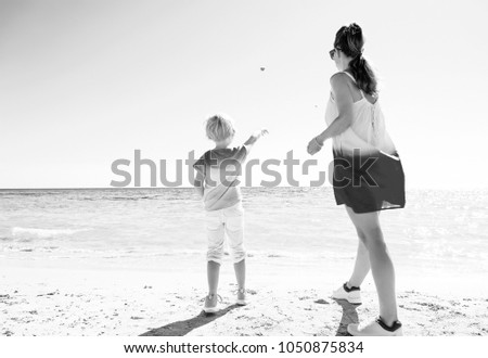 Colorful and wonderfully cheerful mood. Seen from behind trendy mother and daughter in colorful clothes on the seashore throwing stones