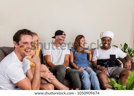 Multinational sports fans laughing and having fun with Russian hat on couch