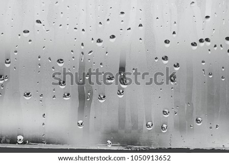 Black and white background of the condensate flowing water on the window glass. Collecting and streaming down. High air strong humidity, large drops drip Royalty-Free Stock Photo #1050913652