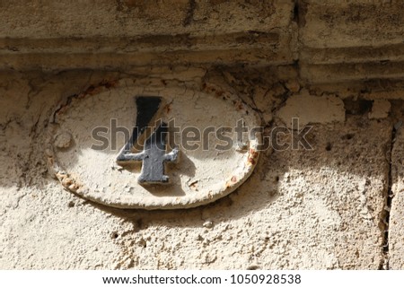 Close up outdoor view of the numver four written in black on a beige oval metallic plate. Numeric sign indicating the address in a french street. Old and rusty element fixed on a stone weathered wall.