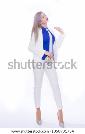 Studio portrait in full length of a beautiful young blond woman with long hair in a white pants suit. A girl in silvery shoes with high heels, in her hands she holds a small silver handbag
