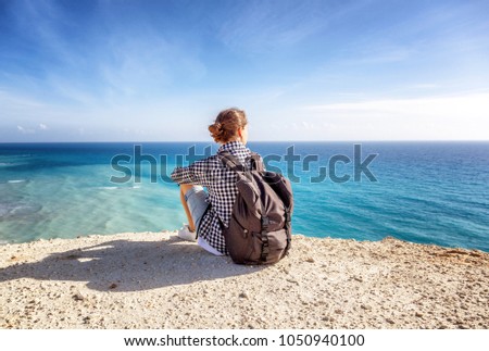 A girl traveler sits on a rock and admires the blue boundless sea, freedom, travel, unity with nature