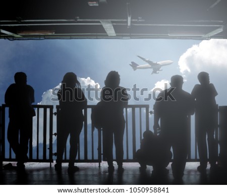 Silhouette of people on an observation deck watching an airplane taking flight.
