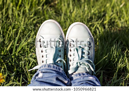 Female legs in a clearing with green grass. Blue sneakers. Spring Park, spring walk.
