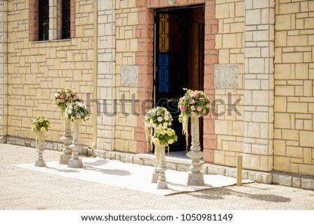 six bouquets of flowers on stands adorn the outsdie of a church
