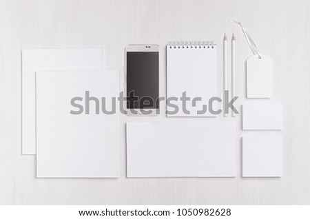 White blank stationery - label, notepad, letterhead, envelop, phone on soft white wooden plank, blank objects for placing your design. Modern stylish work place.