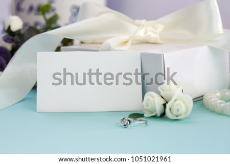 Styled stock photo. Feminine wedding desktop mockup. White roses, box with a bow, engagement ring, beads on pastel blue background. Copy space. Picture for blog