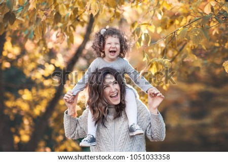 Beautiful young mother spends time with her cute daughter with curly hait in the nature. They have fun and have a walk in the park.