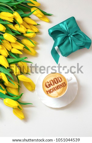 cappuccino in a white cup with an inscription good morning and a bouquet of yellow tulips