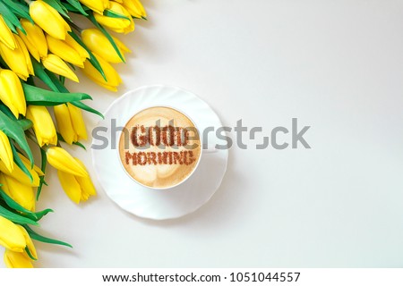 cappuccino in a white cup with an inscription good morning and a bouquet of yellow tulips
