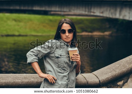 Brunette hipster girl relaxing with coffee against a river in th