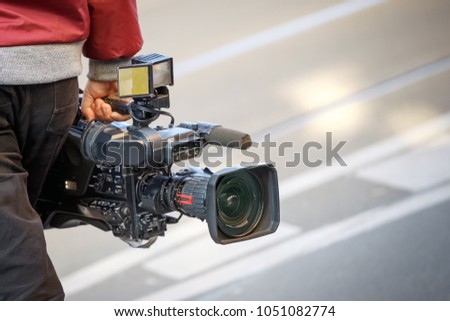 cameraman holding his professional camcorder in the street. Operator in social environment, filming, news outlet, motion-picture cameraman