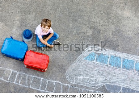 Little kid boy having fun with fast train picture drawing with colorful chalks on asphalt. Child painting with chalk and crayon and going on vacations. Schoolkid sitting on suitcase