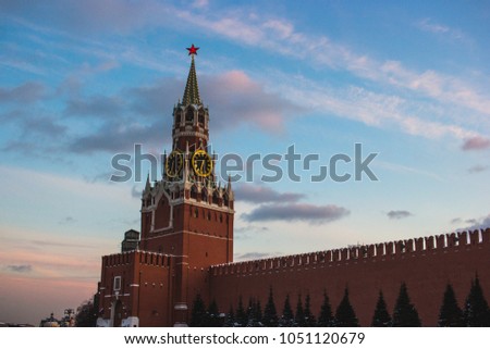 Chiming clock on Spasskaya Tower of the Moscow Kremlin with red brick wall and Fir-trees on blue sky with white and pink clouds background 