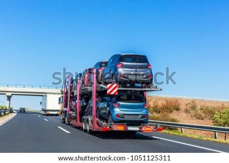 Car carrier trailer with cars on bunk platform. Car transport truck on the highway. Highway bridge. Space for text