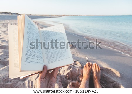 Relax concept. Reading book near the sea - POV. Summer vacations still life. The text is transformed and not recognizable.