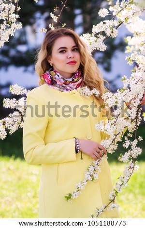 A young woman dressed in a fashionable yellow coat in a flowering park. Standing in a circle of white color.