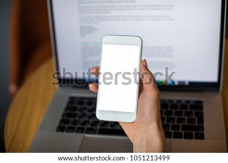 Female professional writer holding mobile phone with mock up empty copy space screen background for advertising text message.Open laptop computer with web site on monitor. Usage cellphone and notebook
