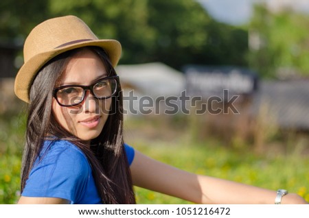 Happy Asians female in cowgirl hat and wear glasses,Sitting on meadow and looking at camera with toothy smile