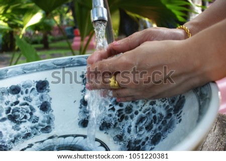 Woman hand washing in ceramic basin surrounded by nature.