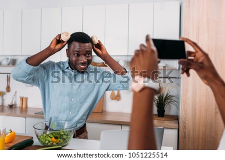 Cropped image of woman taking photo of boyfriend holding mushrooms near head