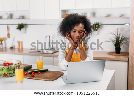 African american woman watching laptop at table in kitchen