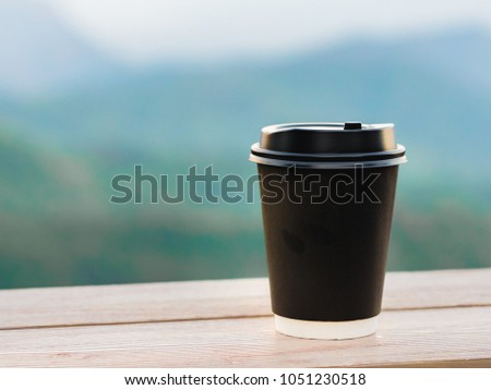 coffee break and relax concept from view from black plastic coffee cup put on wooden table and layer of mountain background