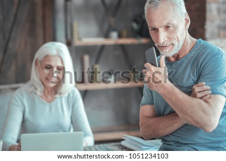 Think about it. Deep unshaken aged man sitting on the table near a woman holding the cellphone and thinking. Royalty-Free Stock Photo #1051234103