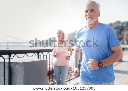 Life is good. Satisfied athletic unshaken man spending time on fresh air looking straight and having cardio exercises on the quay. Royalty-Free Stock Photo #1051239803