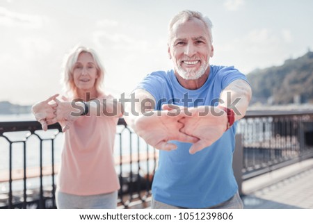 Together is better. Senior pleasant unshaken man standing with a woman smiling and training on the quay. Royalty-Free Stock Photo #1051239806