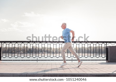 Free of movements. Aged athletic unshaken man being on the quay doing cardio exercises and running. Royalty-Free Stock Photo #1051240046