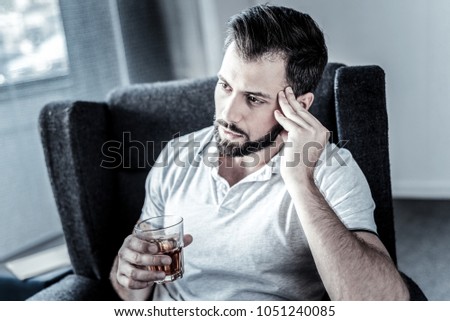 Need to think. Deep unshaken serious man sitting in the chair holding a glass and drinking alcohol. Royalty-Free Stock Photo #1051240085
