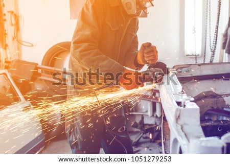 The employee of the service station produces body repair with a welding machine in hand sparks