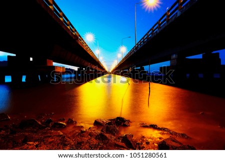 Silhouette long concrete bridge and road lighting flare effect and water reflection on night view shot, Long exposure shot long concrete and lighting with water reflection background on night view.