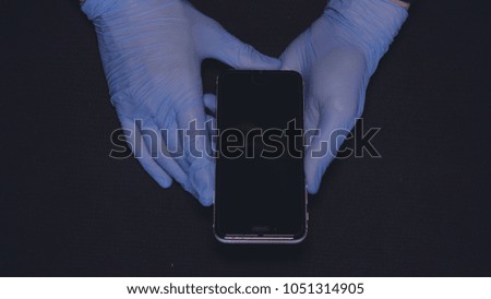 Master in blue rubber gloves, repair mobile phone, black background.	
